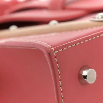 Pink leather bag edge with contrast stitching and round silver snap near strap.