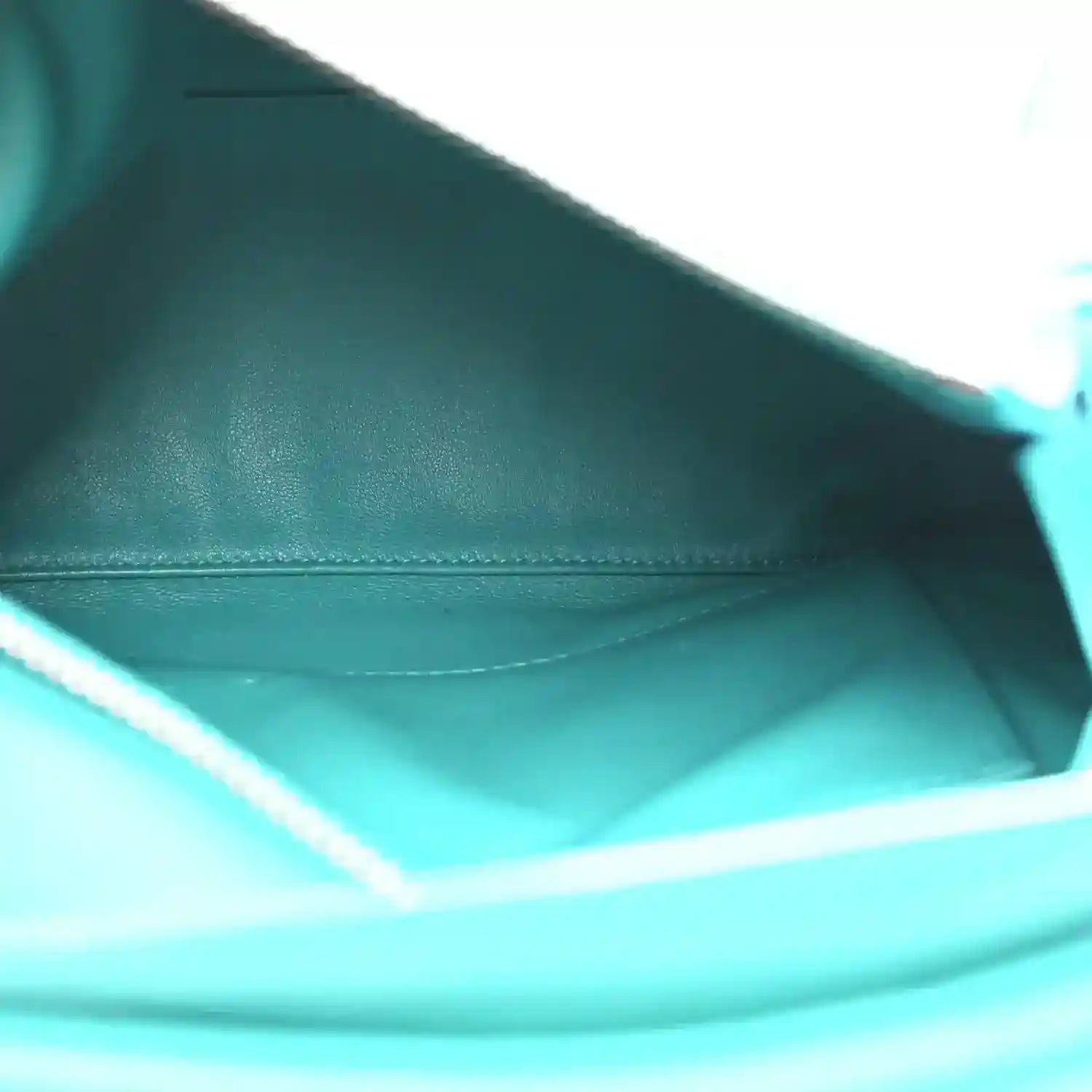 Teal-blue leather interior with stitched seam and smooth lining beneath the zip opening.