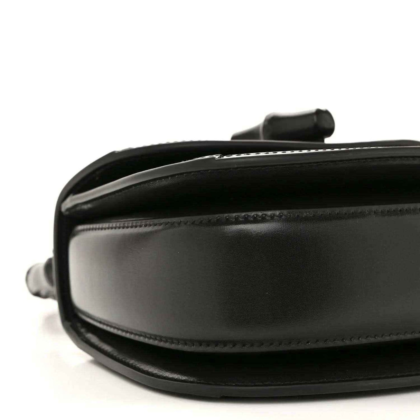 Black mini handbag close-up of side panel with smooth leather and stitching.
