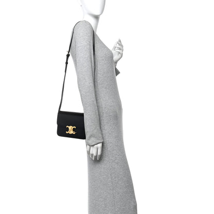 Small black leather crossbody bag on model with gold logo hardware and flap closure.