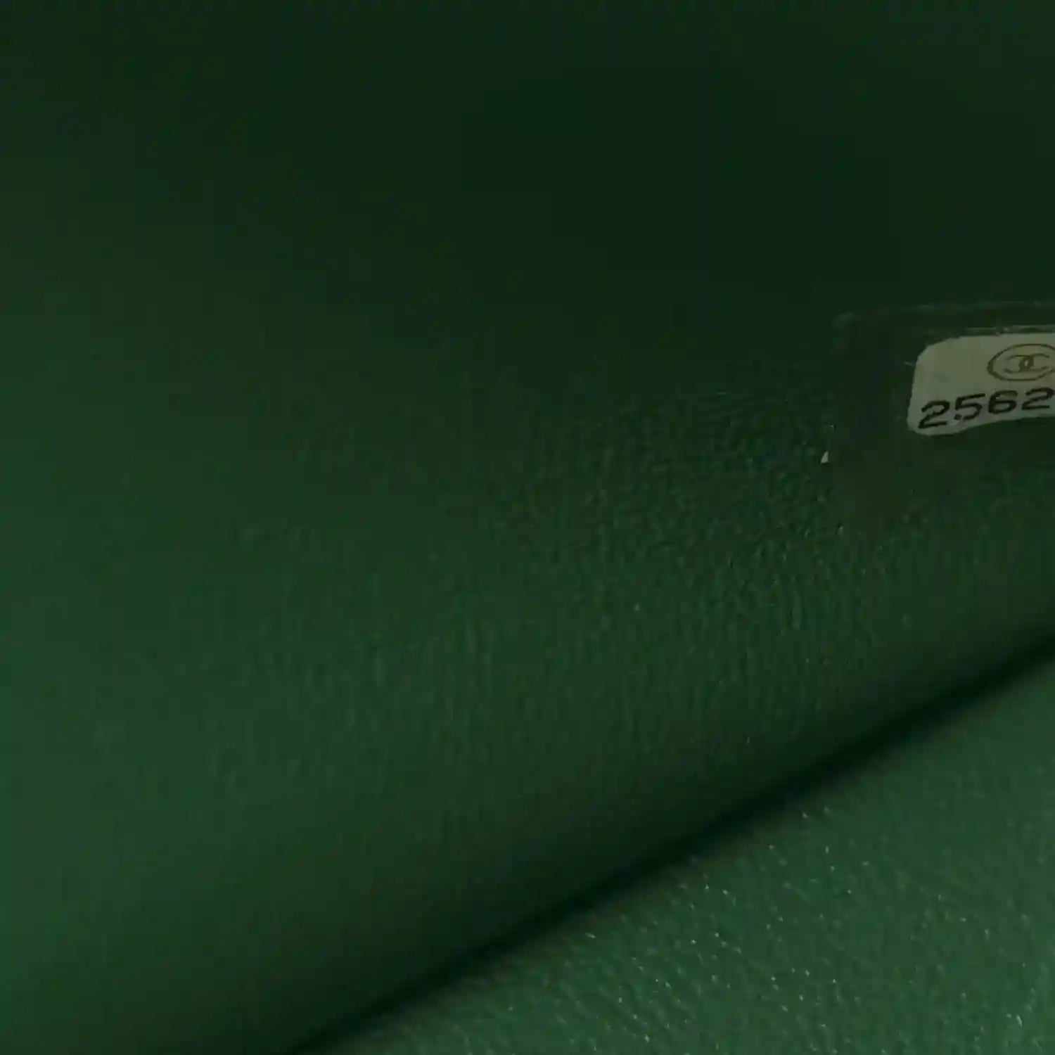 Green leather bag close-up with textured surface and small serial label tag.
