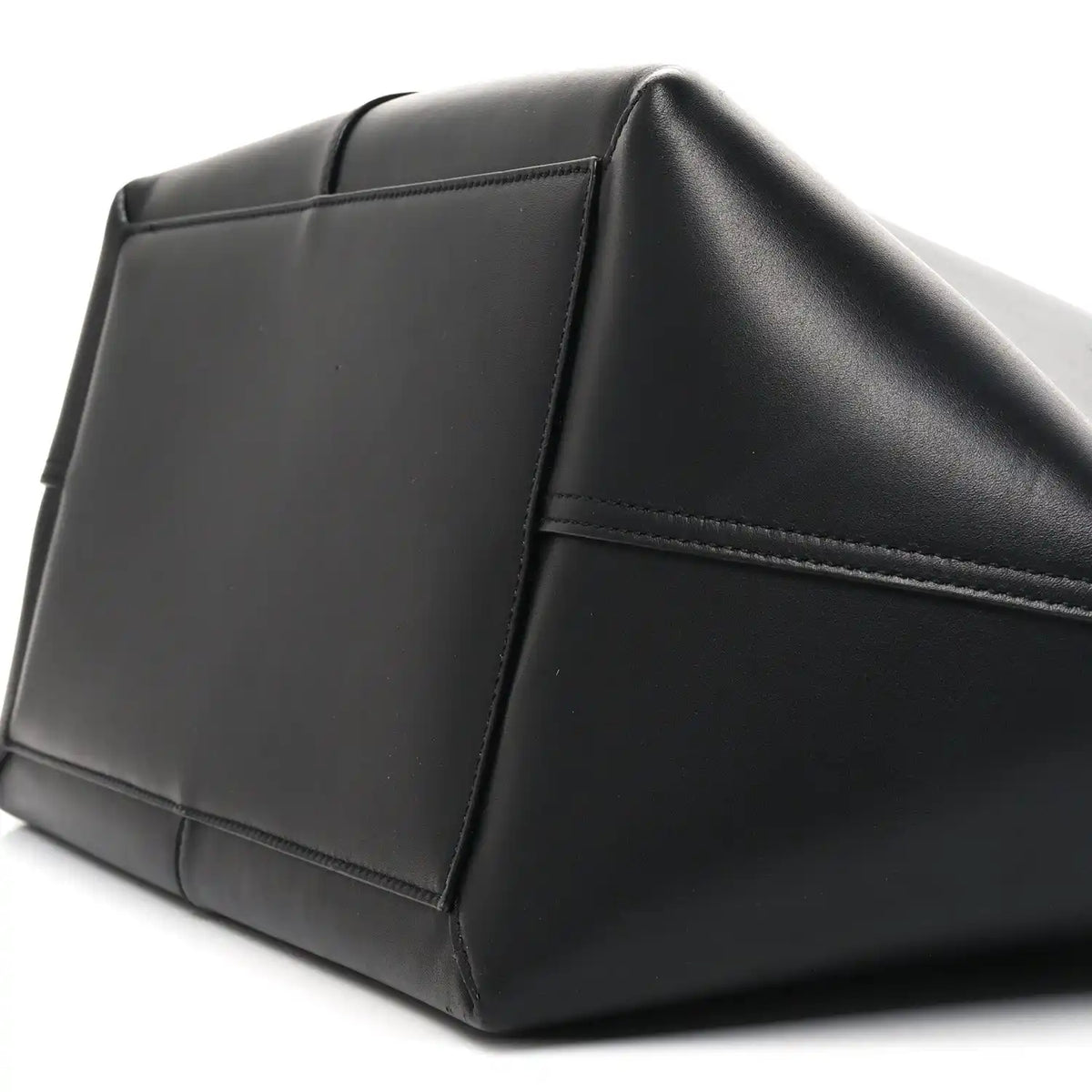 Black smooth calfskin trapezoid tote side panel with stitched seams and curved base