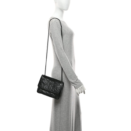 Black mini satchel bag with chain strap and front flap on a small profile