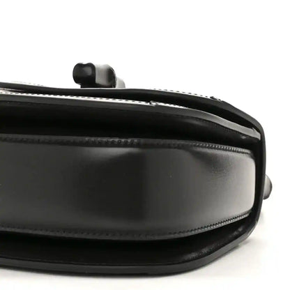 Black mini handbag side close-up with chain handle mount and glossy trim.