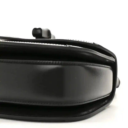 Black mini handbag side close-up with chain handle mount and glossy trim.