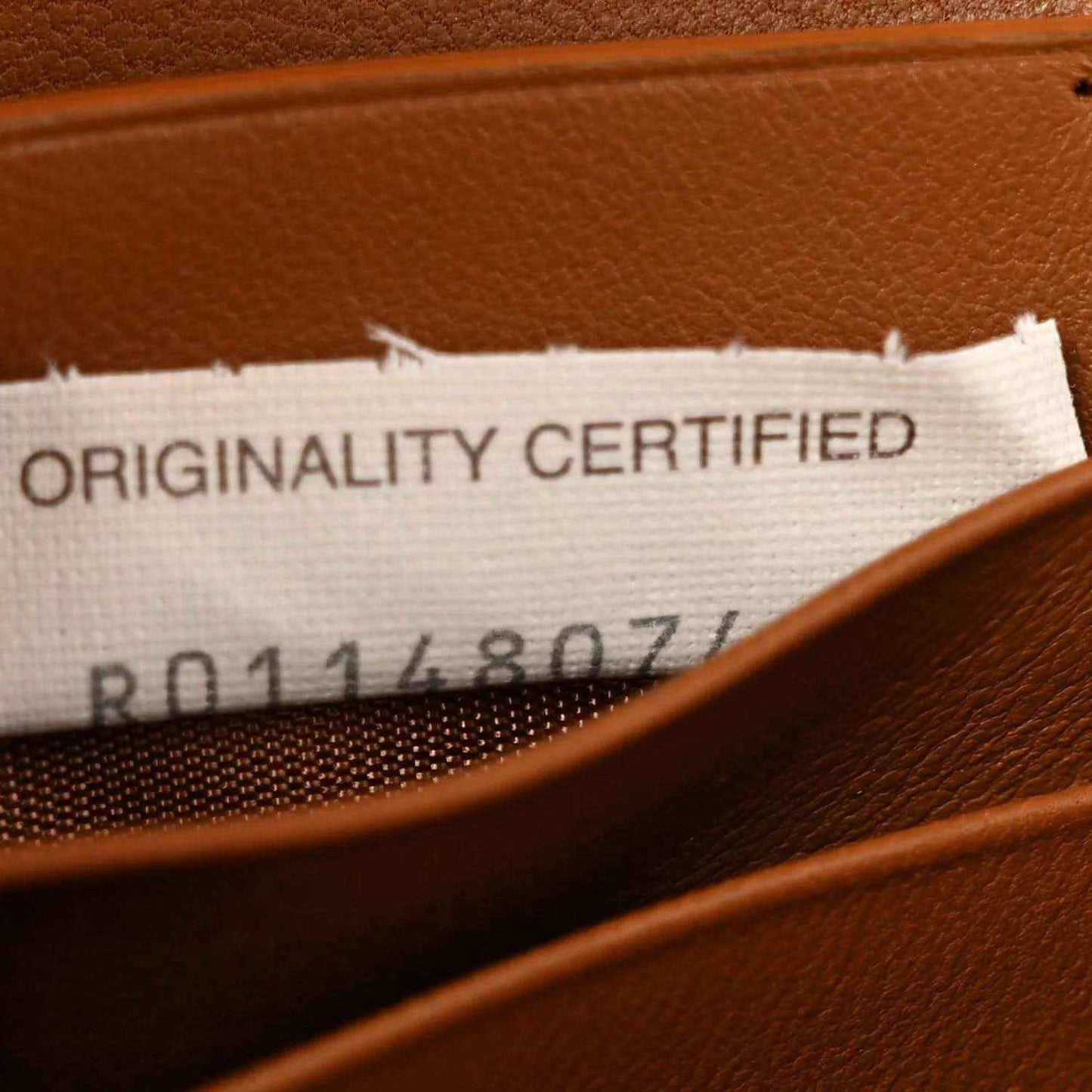 Clutch interior label with text “ORIGINALITY CERTIFIED” beneath stitched trim