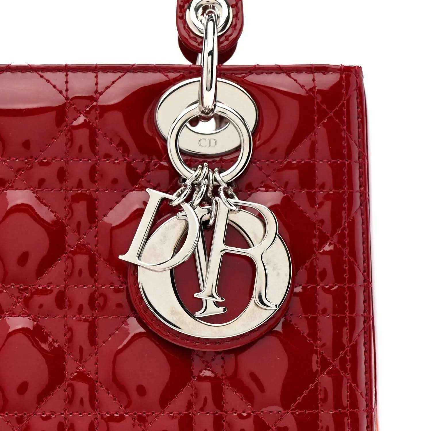Silver CD monogram charm on red patent leather handbag front.