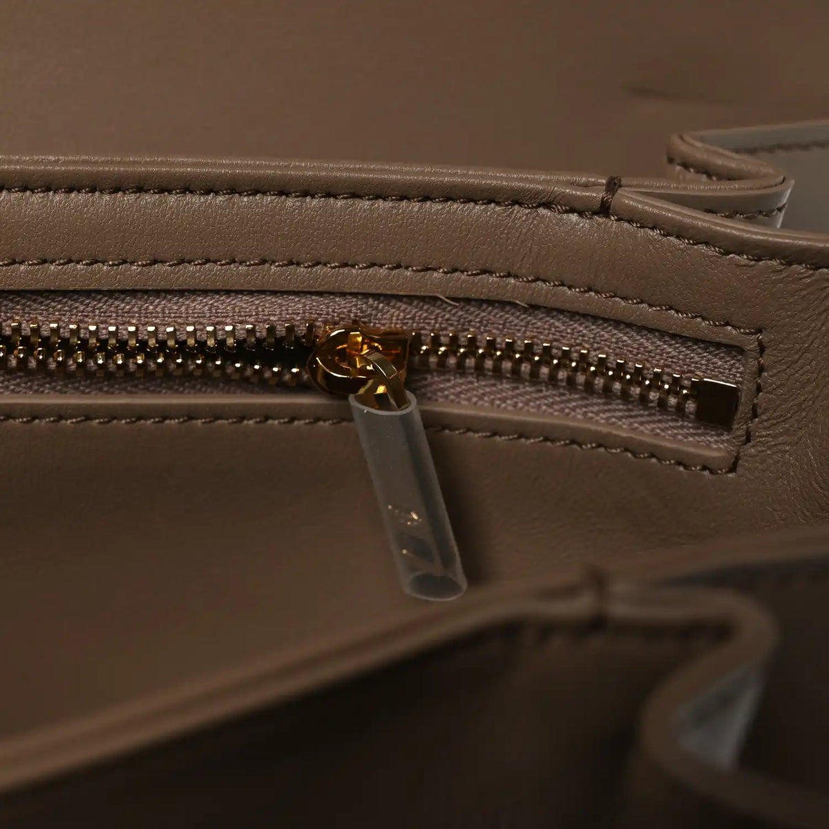 Shiny brown leather bag close-up of gold-tone zipper and clear zip pull