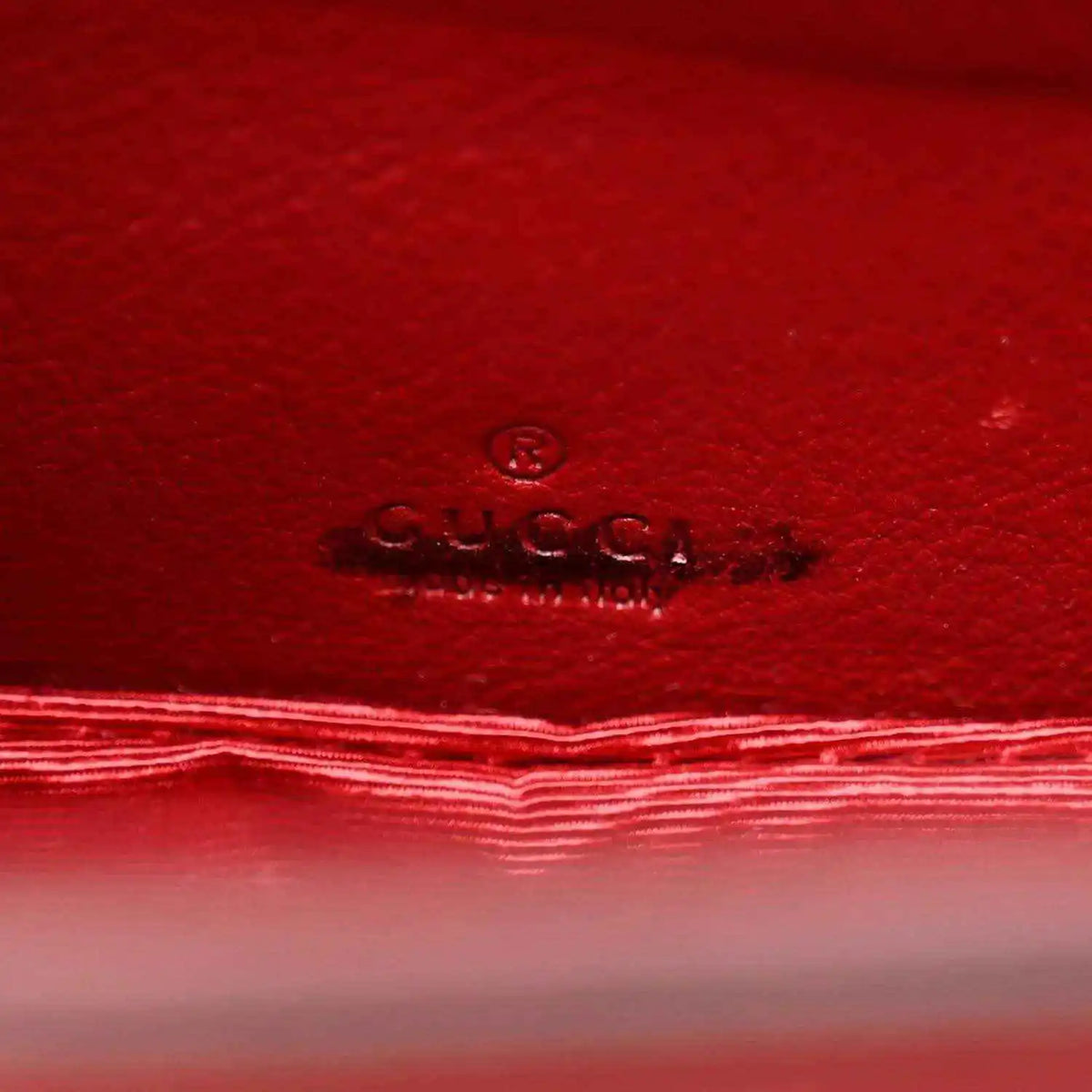 Red leather interior panel with embossed Gucci logo and stitched border.