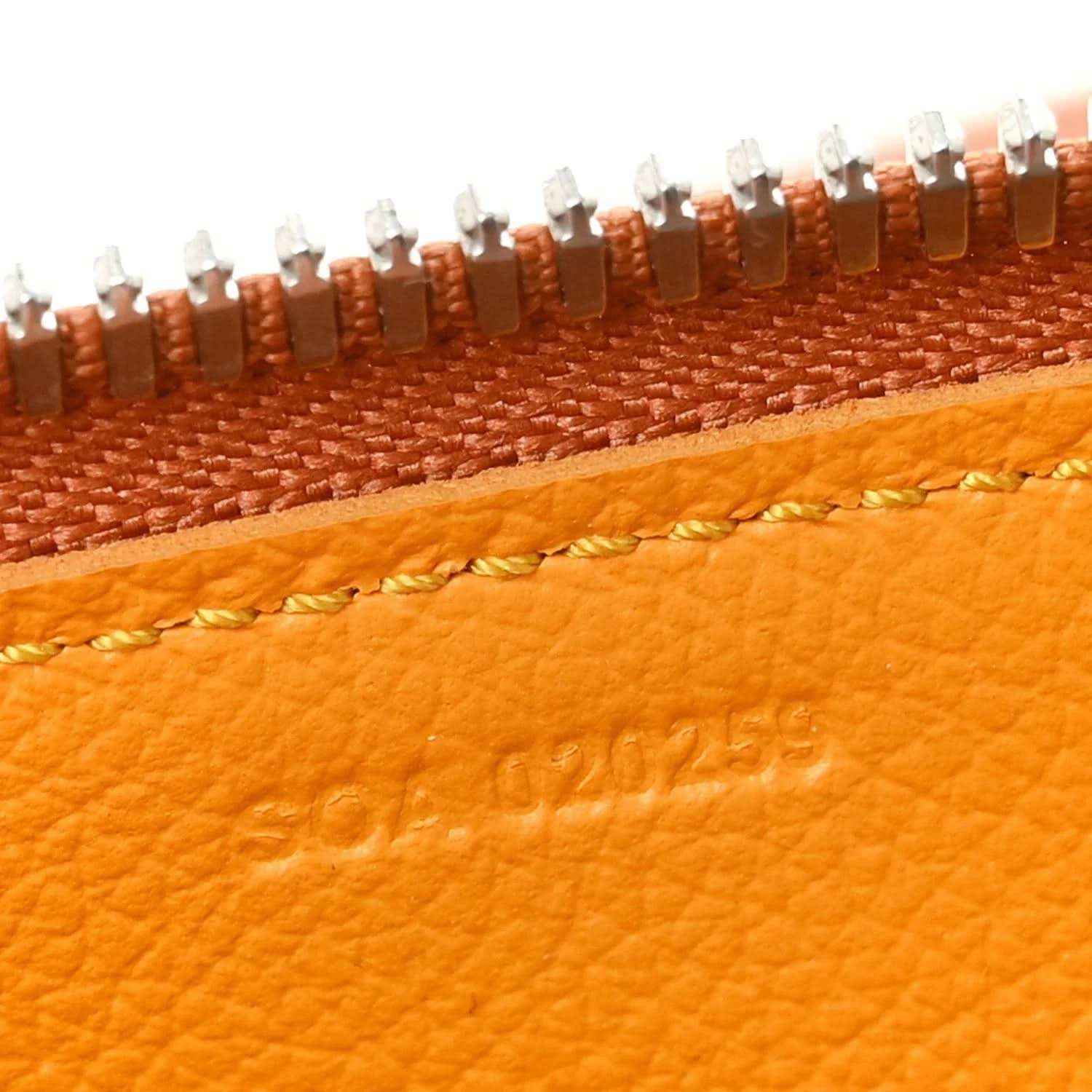 Close-up of orange leather edge and stitched Goyardine logo with metal teeth trim