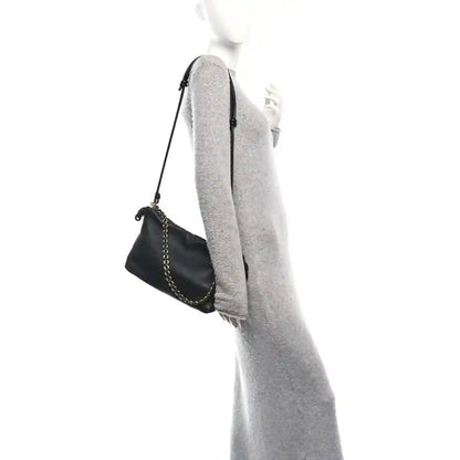 Black leather mini clutch with chain strap, shown from side on a model.
