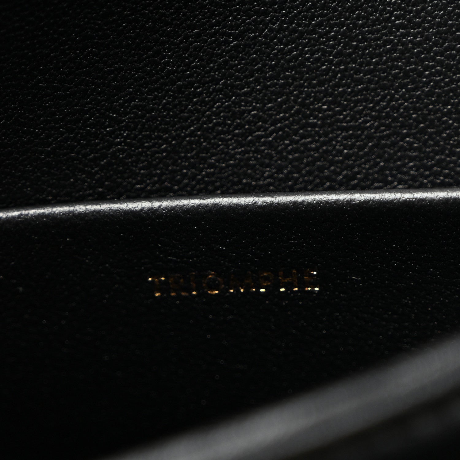 Close-up of black leather with faint embossed logo on bag panel.
