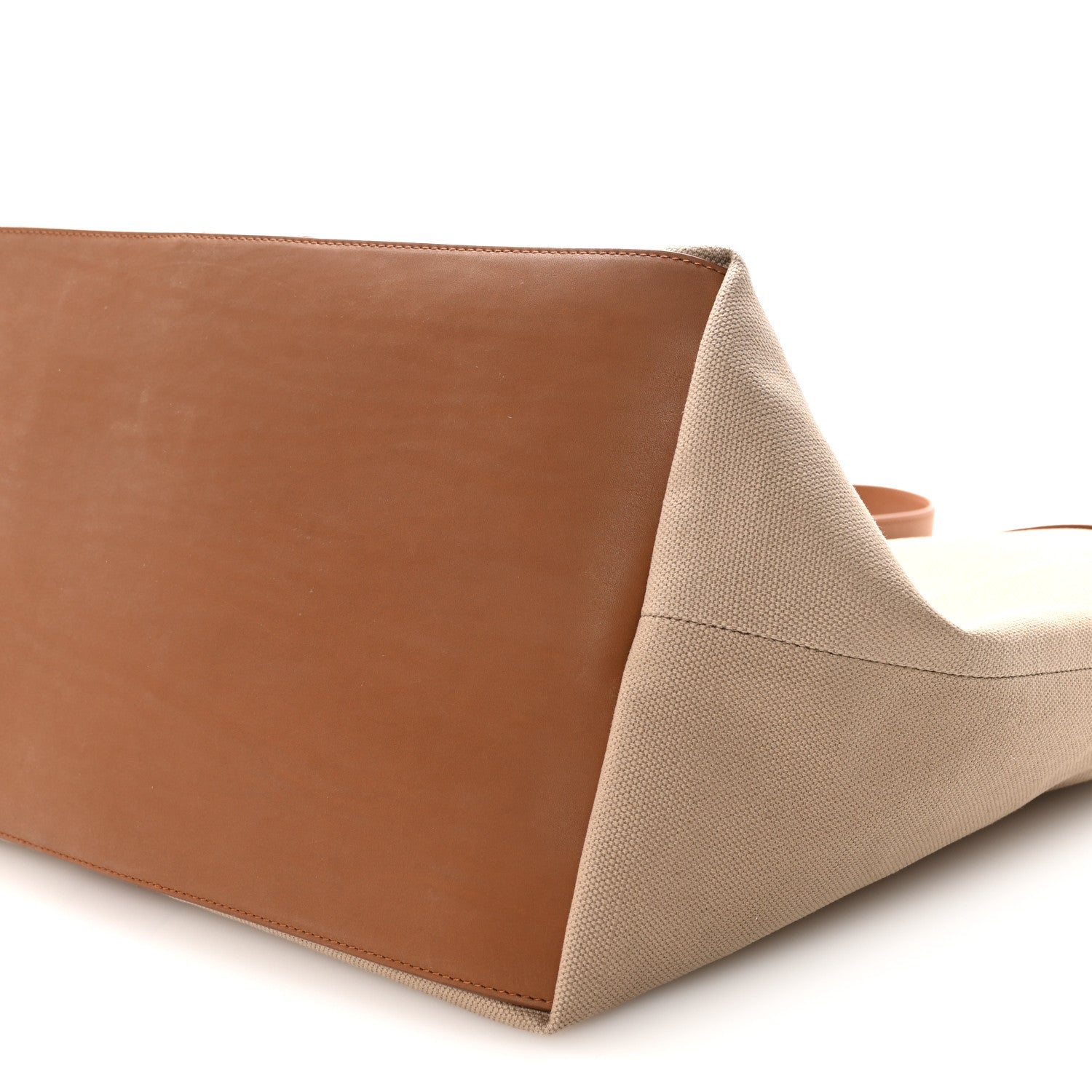 Tan canvas tote side with brown leather bottom panel, close-up