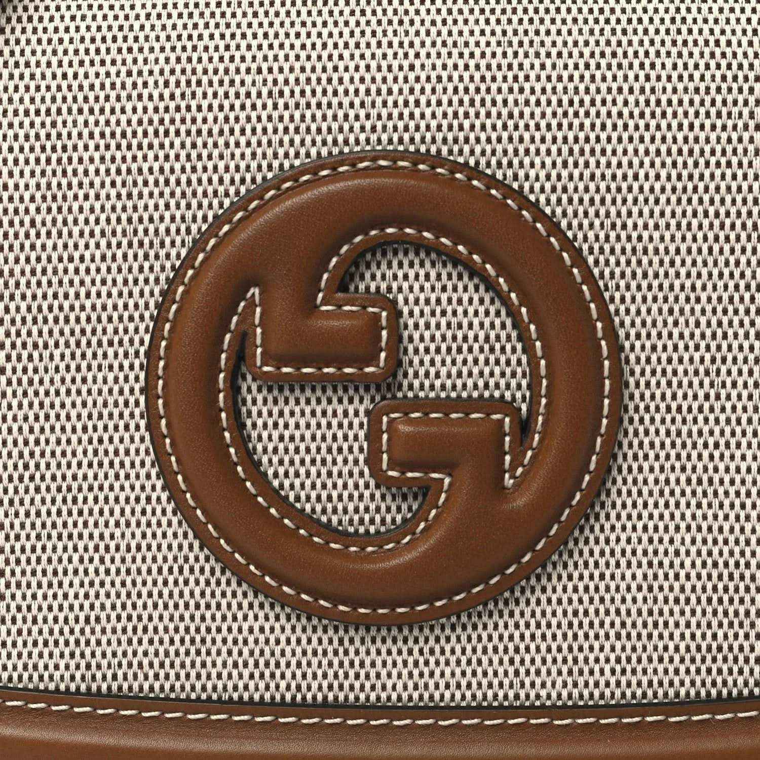 GG logo emblem on beige textured canvas with brown leather border and stitching