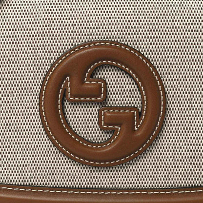 GG logo emblem on beige textured canvas with brown leather border and stitching