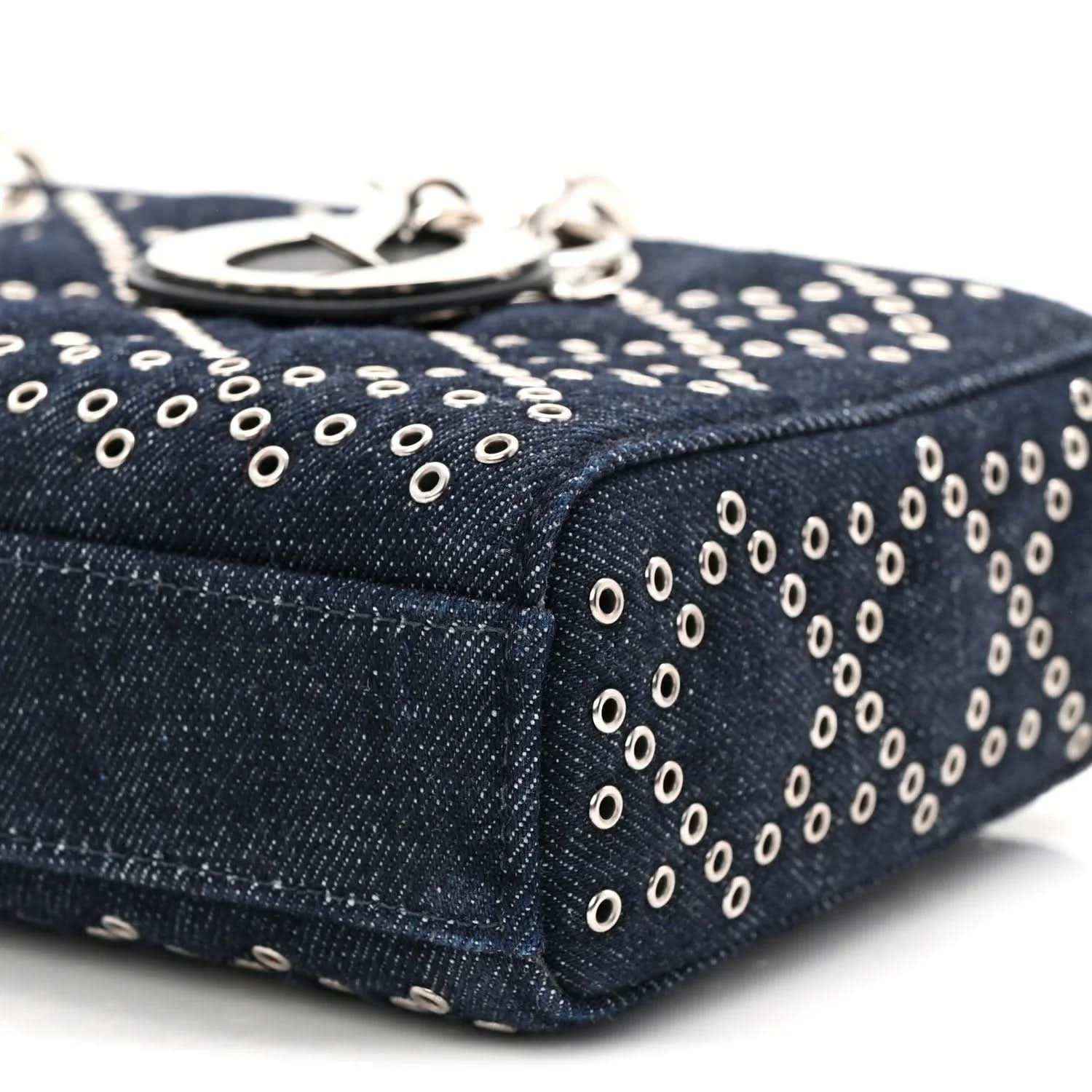 Dark blue denim handbag top edge with silver-tone eyelet pattern and zipper pull