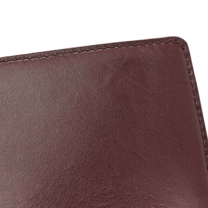 Dark burgundy leather clutch corner with clean edge stitching and textured grain