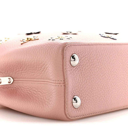 Pink leather handbag side with snap buttons, stitched trim, and small metal studs
