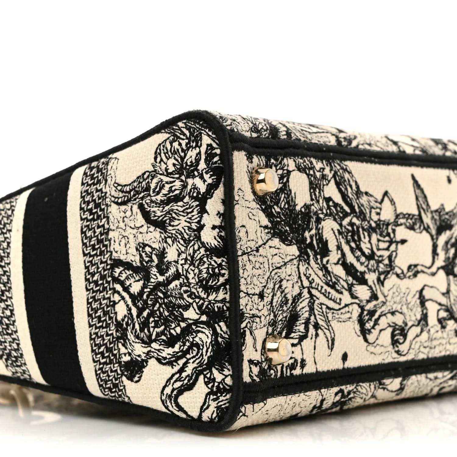 Toile-printed tote side panel with gold hardware studs and black trim stripe.