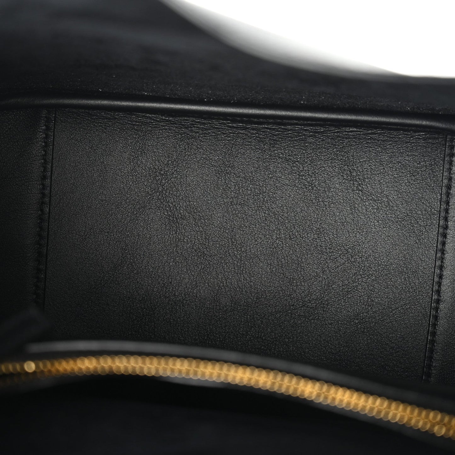 Close-up of black leather bag with gold-tone zipper teeth along the top edge.