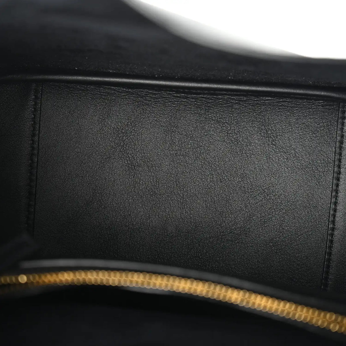 Close-up of black leather bag with gold-tone zipper teeth along the top edge.