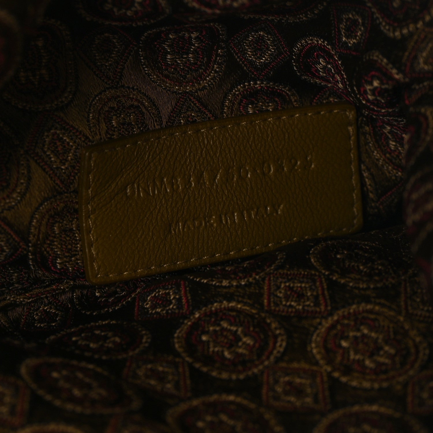 Leather logo tag on jacquard medallion fabric, brown/olive, embossed lettering.