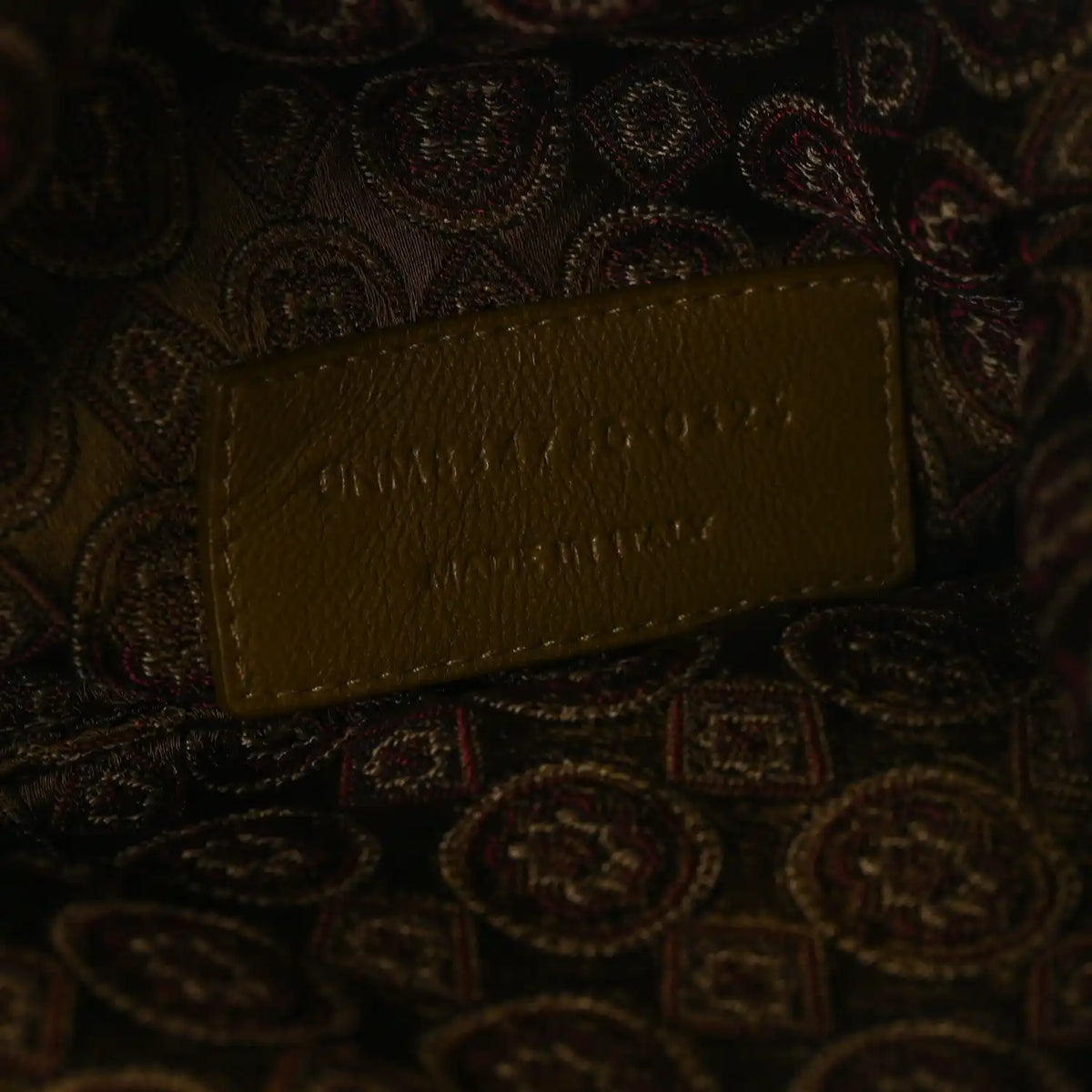 Leather logo tag on jacquard medallion fabric, brown/olive, embossed lettering.