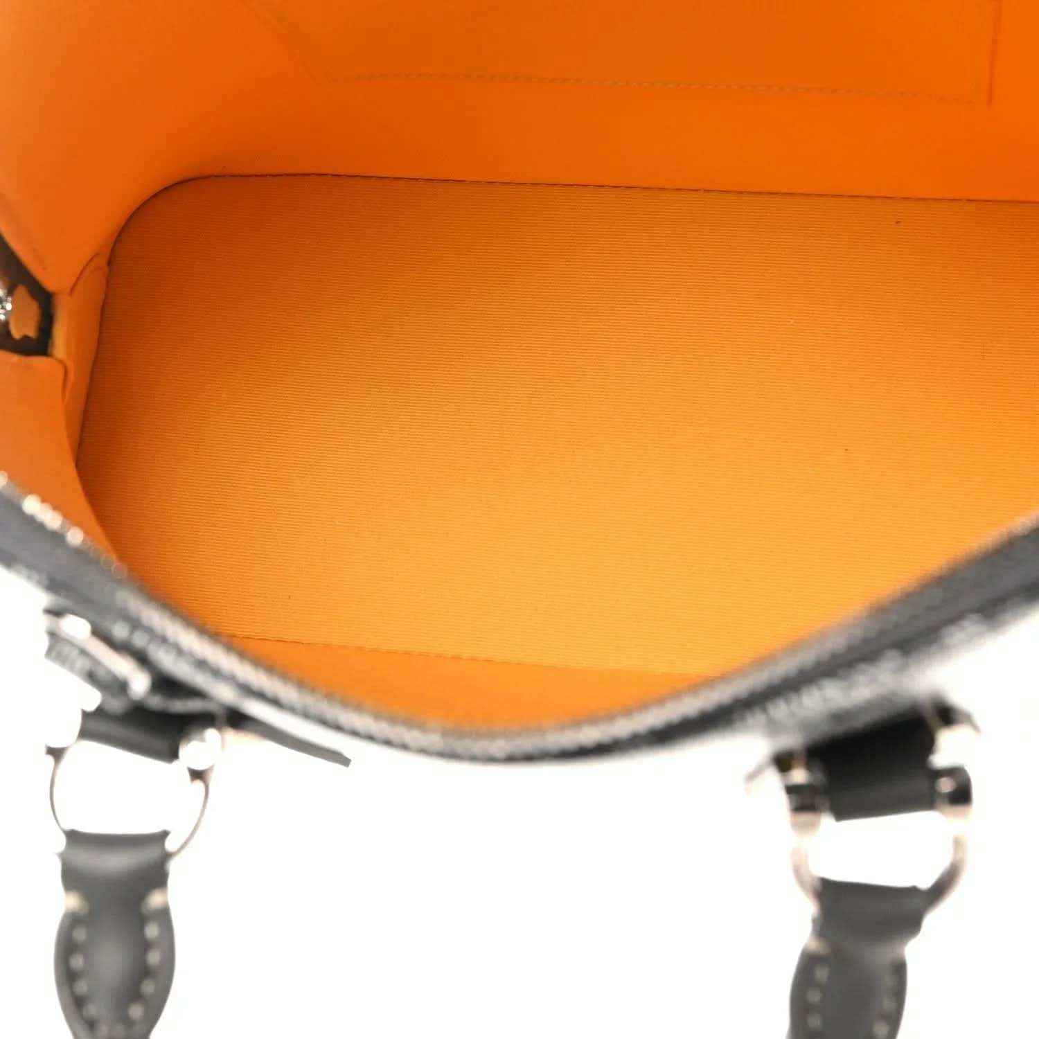 Handbag interior with bright orange lining and dark leather trim at top opening.