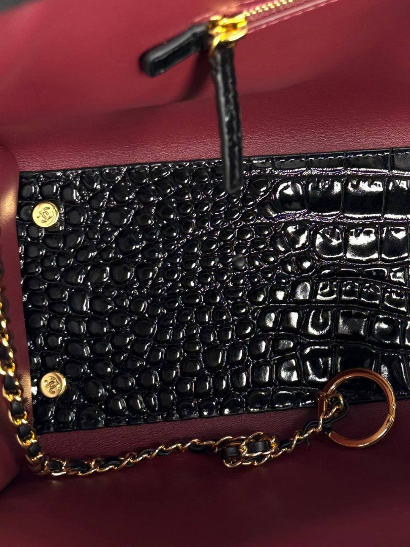 Close-up of black croc-embossed small bag with gold chain and burgundy interior panel
