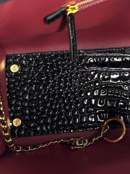 Close-up of black croc-embossed small bag with gold chain and burgundy interior panel