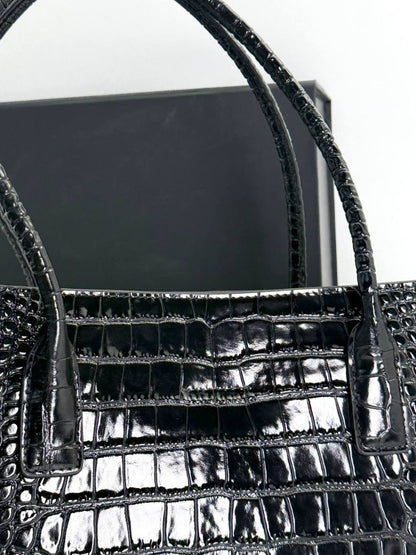 Close-up of black croc-embossed shopping tote front with structured panel and handle base