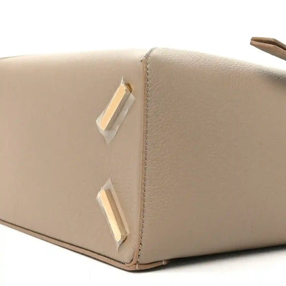 Sand leather bag corner with vertical gold-tone hardware and curved top edge stitching.