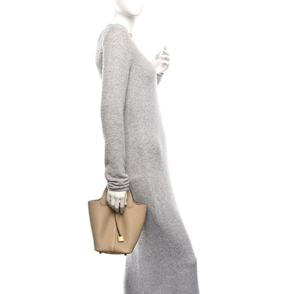 Beige leather mini tote bag with gold lock closure, held by the top handles