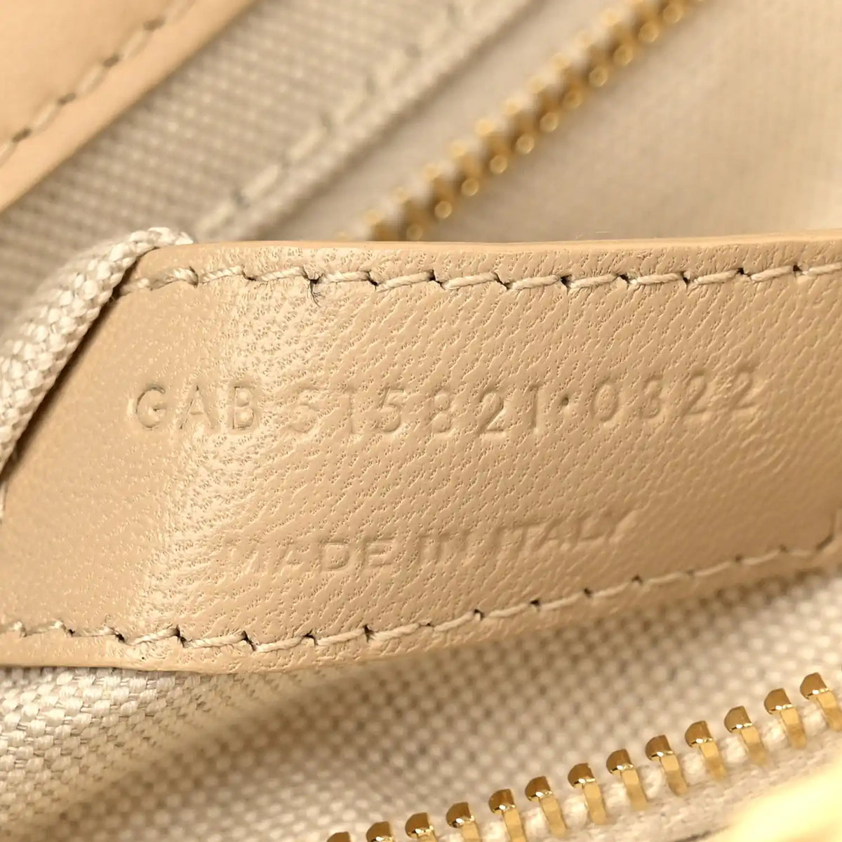 Beige leather strap end with embossed code and stitched trim