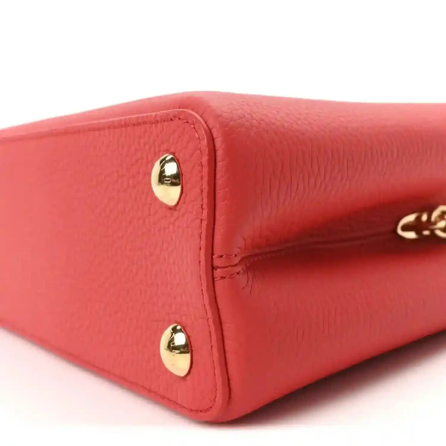 Red leather mini handbag corner with gold stud hardware and stitched edge detail.