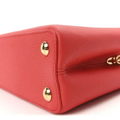 Red leather mini handbag corner with gold stud hardware and stitched edge detail.