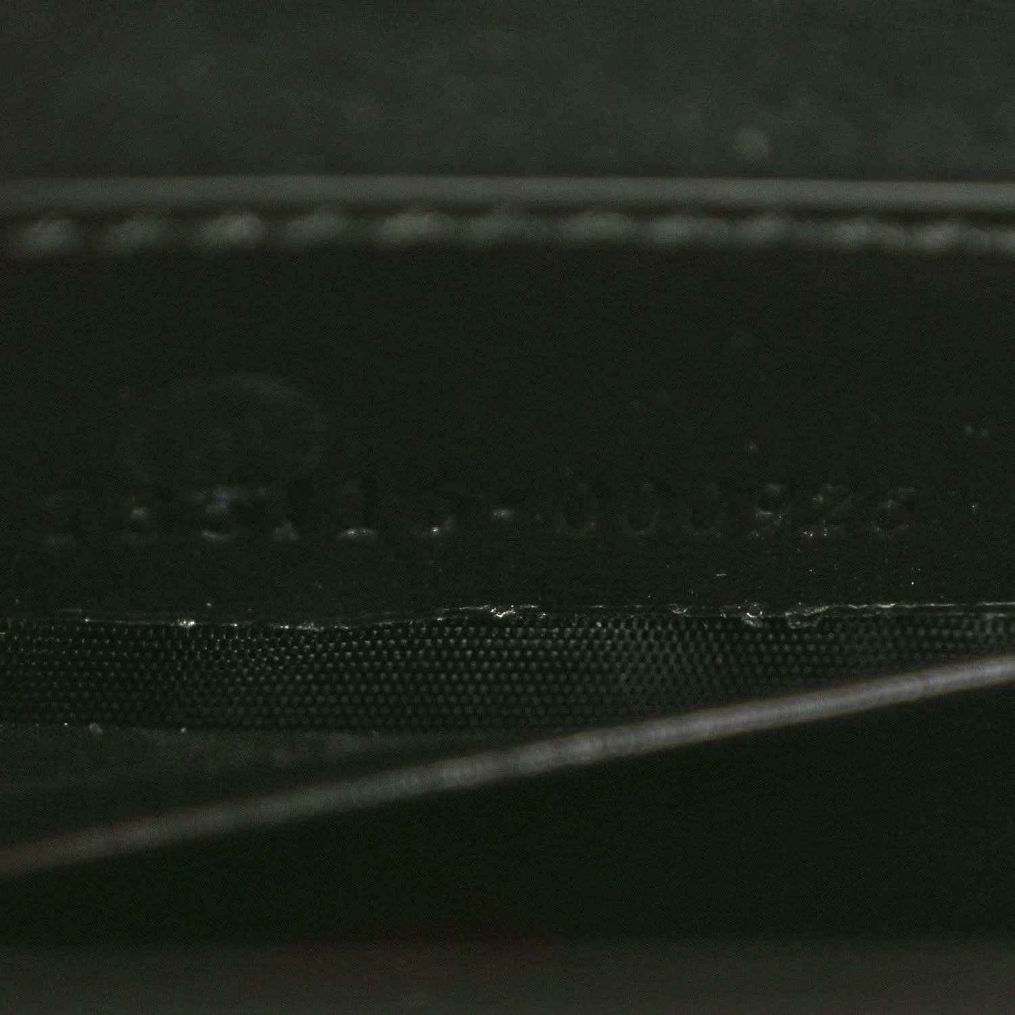 Black handbag close-up of textured leather panel and stitched edge.