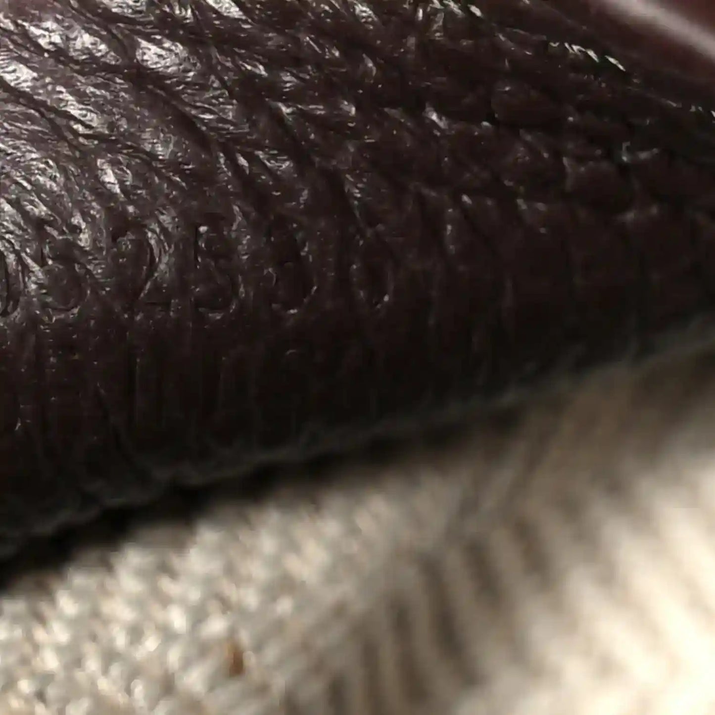 Dark chestnut grained leather close-up with textured surface and stitched edge
