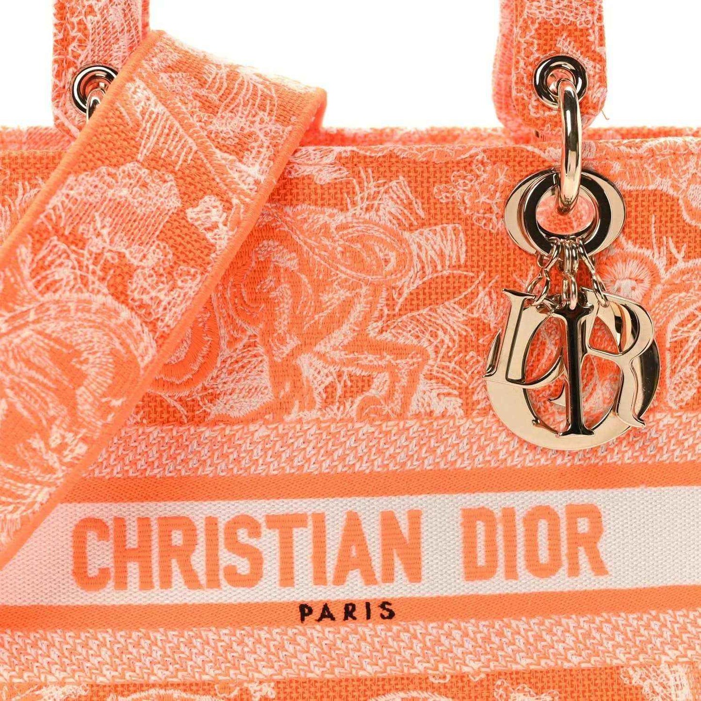 Orange embroidered tote bag close-up with Dior logo ribbon and silver-tone charm.