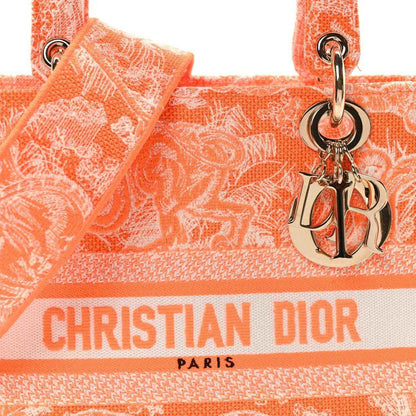 Orange embroidered tote bag close-up with Dior logo ribbon and silver-tone charm.