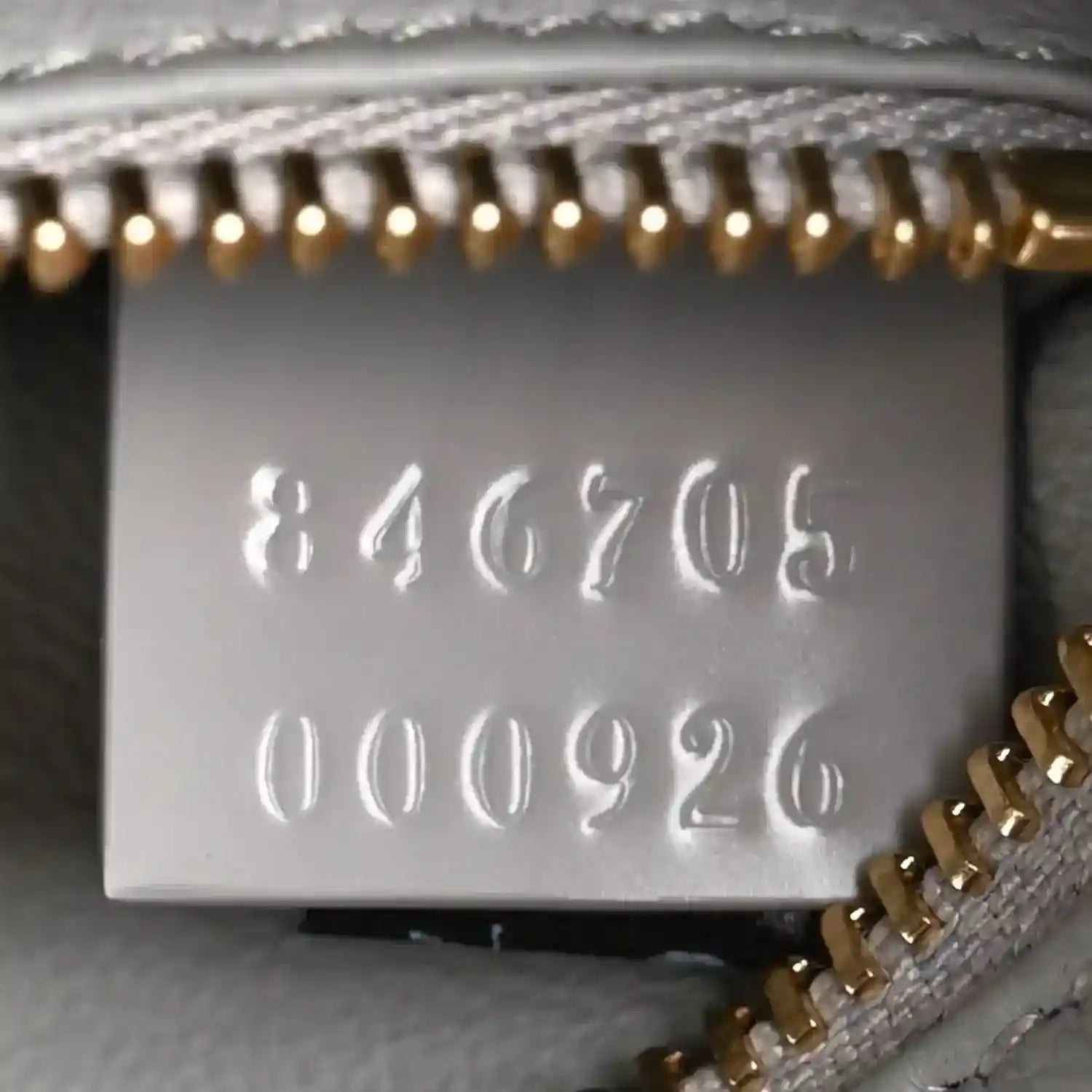 White inner label with stamped numbers and a gold-tone chain accent