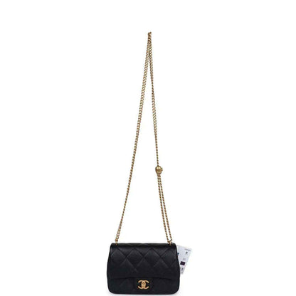 Black quilted mini flap bag on long gold chain strap.