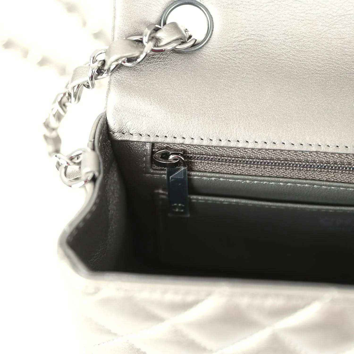 Silver flap bag interior with zipper, stitching, and chain attachment ring
