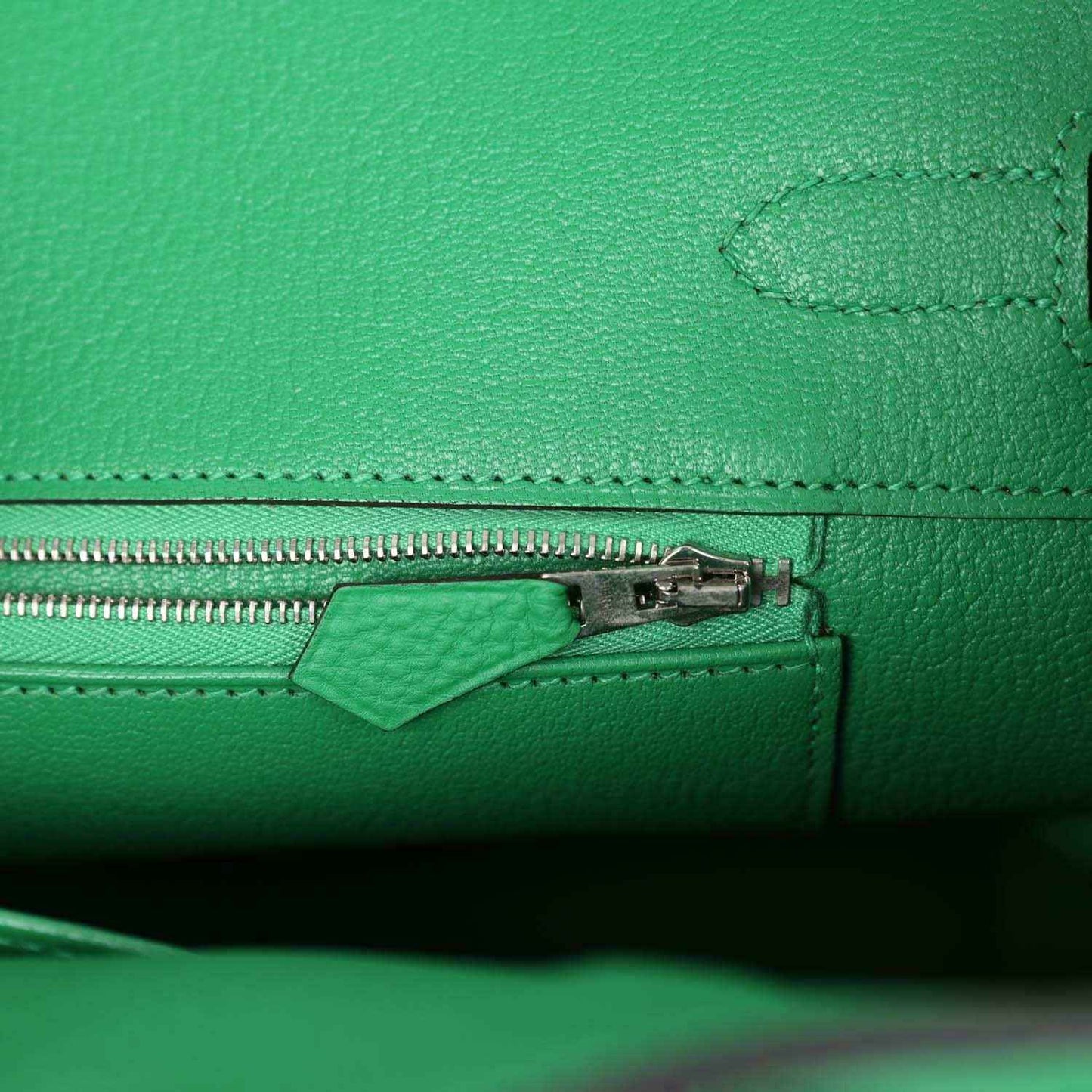 Green leather handbag close-up of zipper pull and stitched seam detail