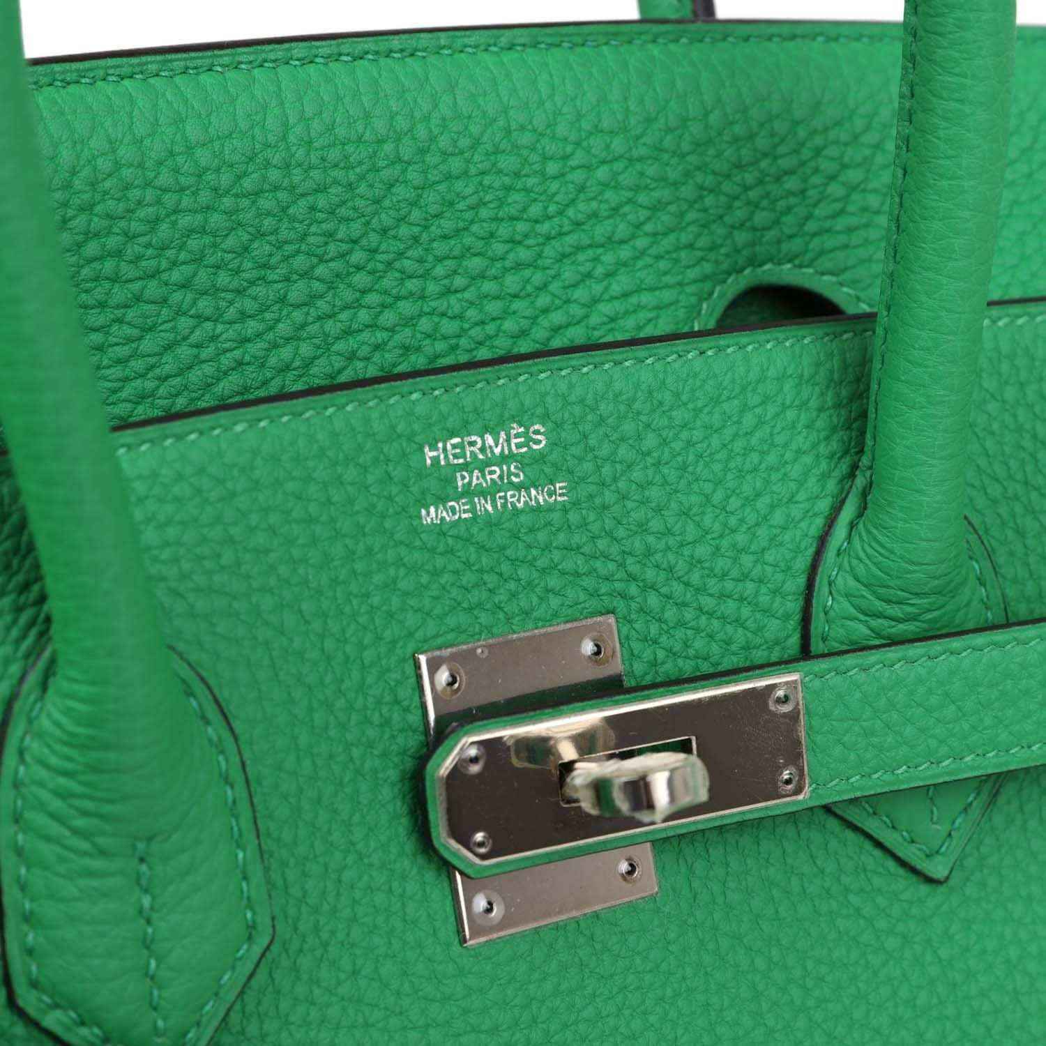 Green leather handbag close-up of metal lock plate and leather strap stitching