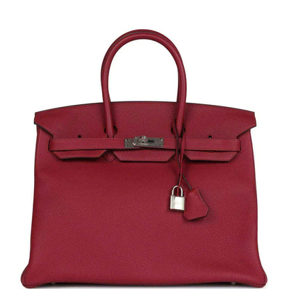 Red leather Birkin-style handbag with top handles, front flap, and hanging padlock charm