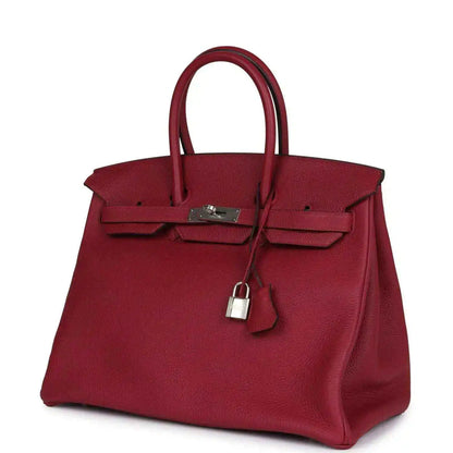 Red leather Birkin-style handbag with front clasp and hanging padlock charm, angled view