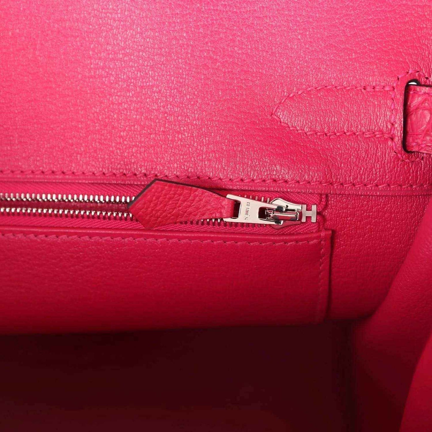 Pink Birkin handbag zipper close-up with metal pull and stitched panel.