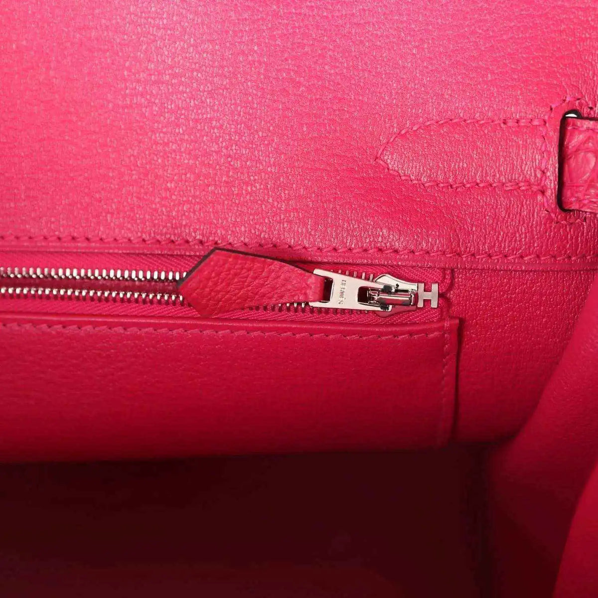 Pink Birkin handbag zipper close-up with metal pull and stitched panel.