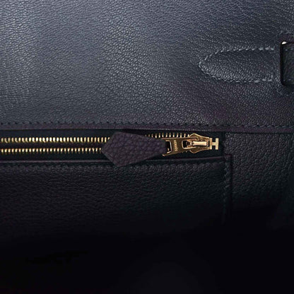 Leather handbag zipper close-up with gold teeth and small leather pull tab, dark color